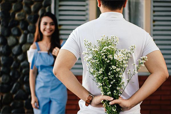 man is hiding flowers over his back from woman
